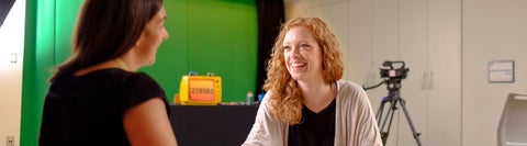 Two women talking in front of a green screen