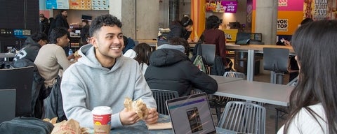 Student laughing and enjoying a Tim Hortons wrap and hot drink. 