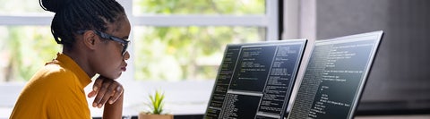 Person working at a desk, looking at two monitors displaying code.
