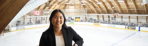 Student in black blazer stands in an arena with a hockey rink in the background