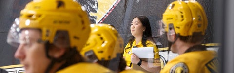 Student holding a clipboard with hockey players in the foreground
