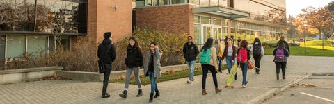 Several students walk past a brick and glass building at the University of Waterloo