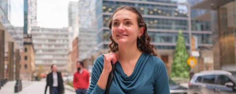 A student standing in a downtown area holding the strap of their bag