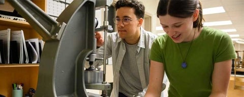 Engineering students using a materials testing machine in a lab.