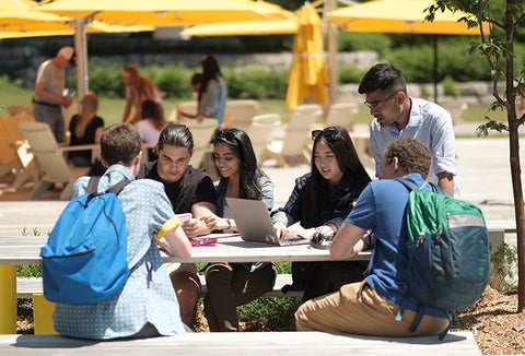students sitting at a picnic table on campus on a sunny day