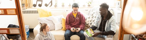 three students sitting together in a dorm room