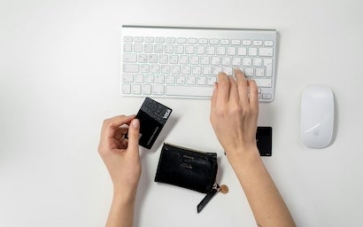 A hand typing on a keyboard with a credit card being held on the other hand.