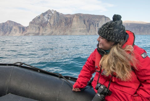 student sitting a zodiac boat on open water with mountain behind