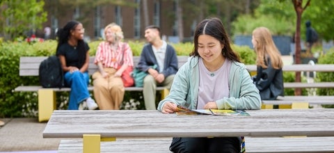 A student reading a brochure while sitting at a picnic bench 