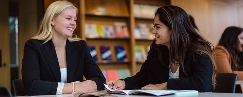Two students in business wear sitting at a table smiling 