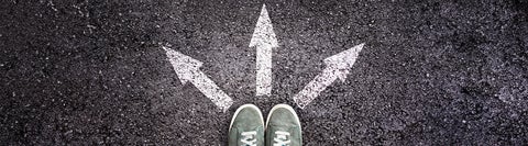 feet standing on road over three directional arrows