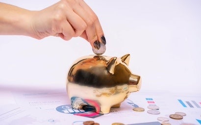 A hand putting a coin in a gold piggy bank.