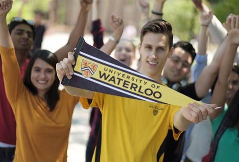 student holding Waterloo pennant in front of happy crowd with raised hands