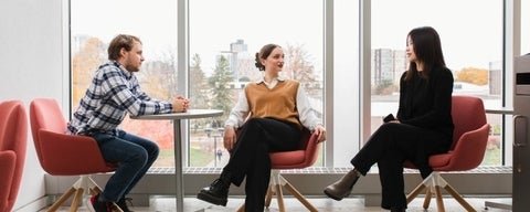 Three students dressed professionally sitting on chairs and talking.