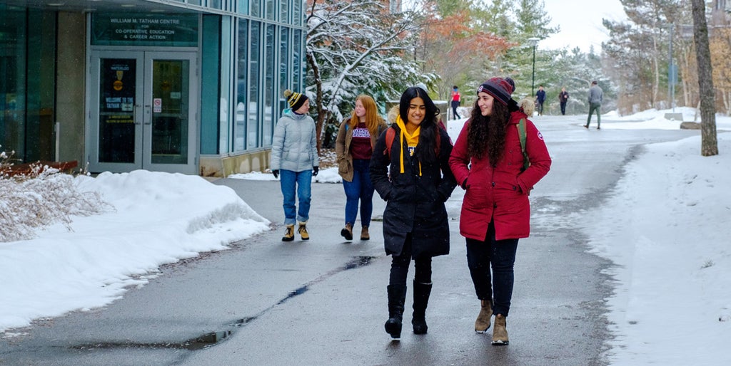 Students in winter coats walk along snowy path at the University of Waterloo