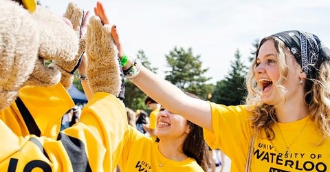 Student in gold short high-fives the Waterloo mascot