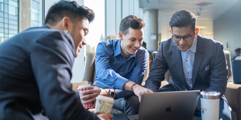 Group of young men in suits looking at a laptop.