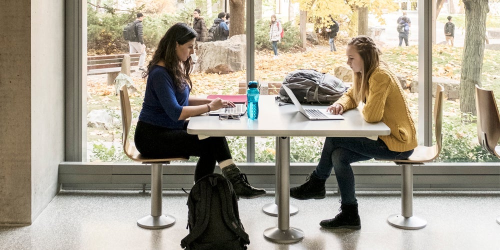 2 girls study in front of window.