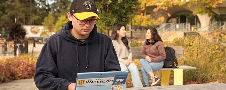 Student sitting outside at a wooden table typing on their laptop