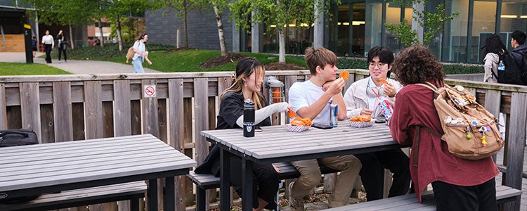 Four students sitting on a patio eating burgers and fries