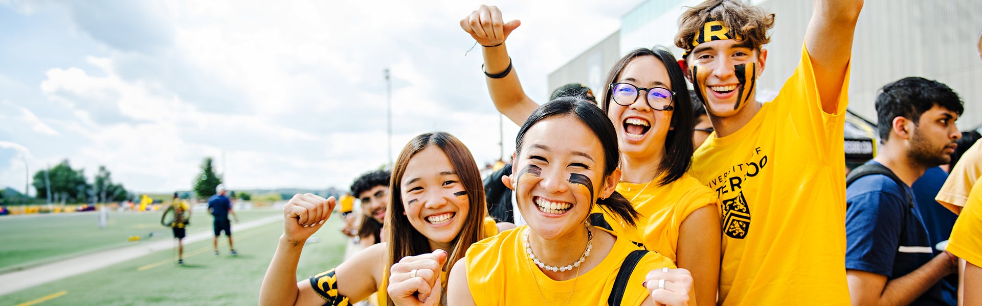 Students in gold shirts and wearing face paint cheer at the camera