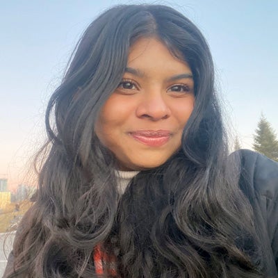 Student with dark hair and wearing a winter coat smiles at the camera