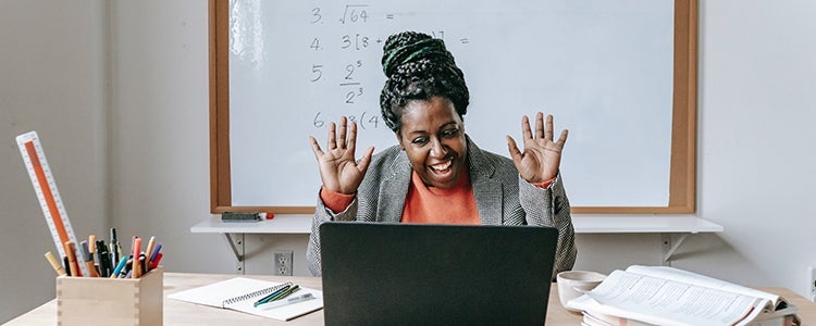  A teacher sitting at their desk on a video call. Their expression is excited and their hands are up.