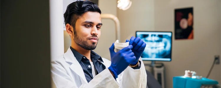 student in lab coat looking at model teeth