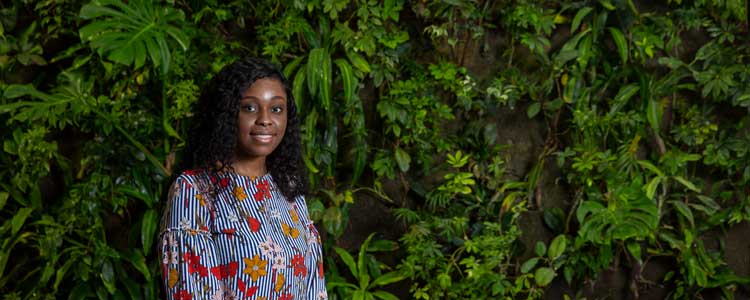 Okeoghene standing infront of a wall covered in plants