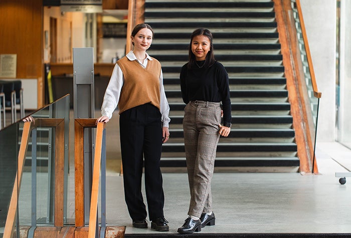 Two students walking down a staircase dressed in business casual clothing