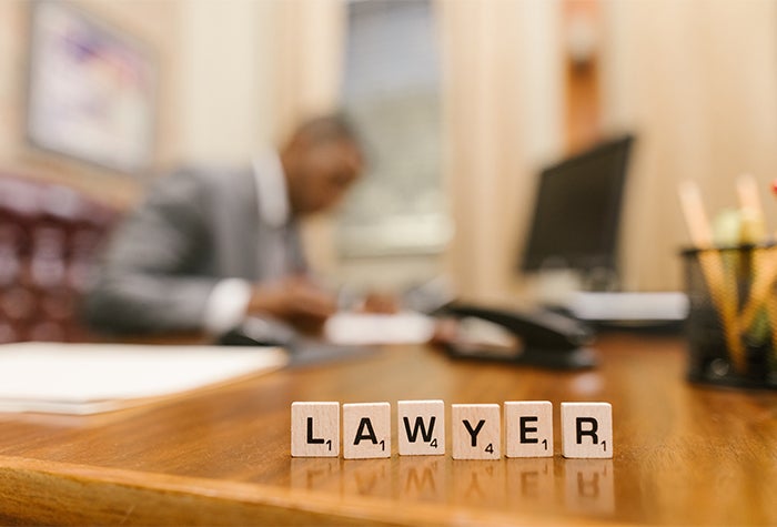 A lawyer in Canada working at their desk. Sitting on their desk are wooden block letters that spell out the word lawyer