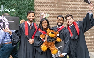 A group of new graduates celebrate holding a teddy bear