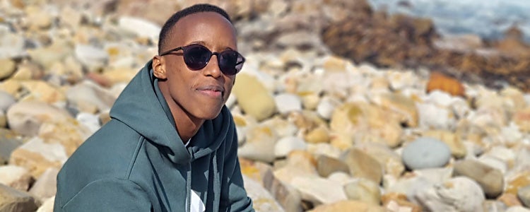 Student wearing a green sweater sits on rocks looking at the camera