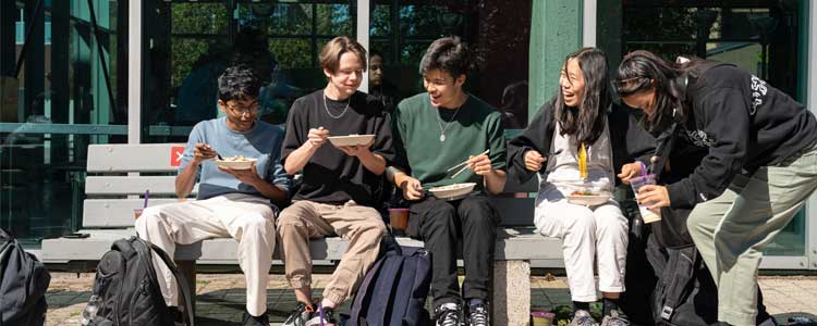 Group of students eating on a bench together. 