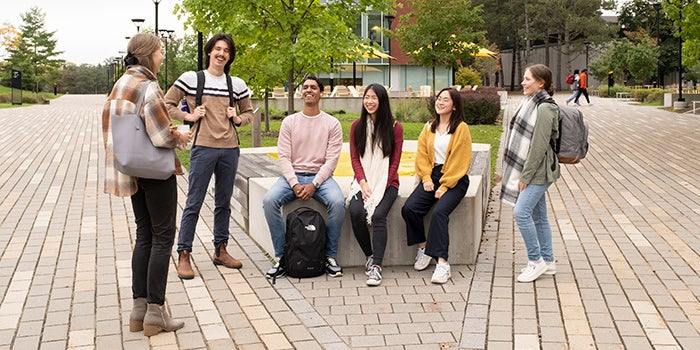 Group of six students sitting outside chatting with each other