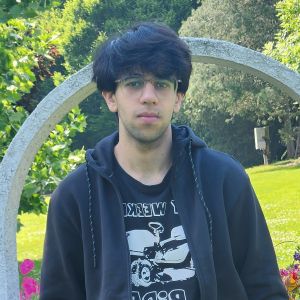 Dayyan wears an unzipped sweater and glasses in a garden