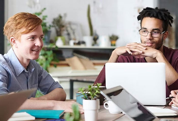 Students study together at a table with their laptops