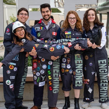 Group of students in overalls holding another student in their arms