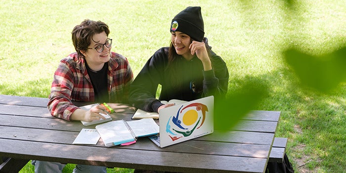 Two students sitting outside at a picnic table, chatting