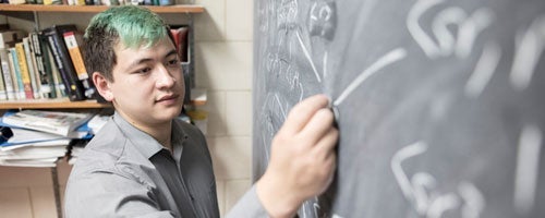 Math student solving equations on a chalkboard