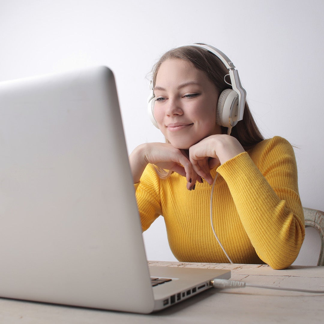 Student weating a yellow shirt sitting at a laptop with headphones on