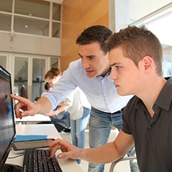 Two men look intently at a computer monitor