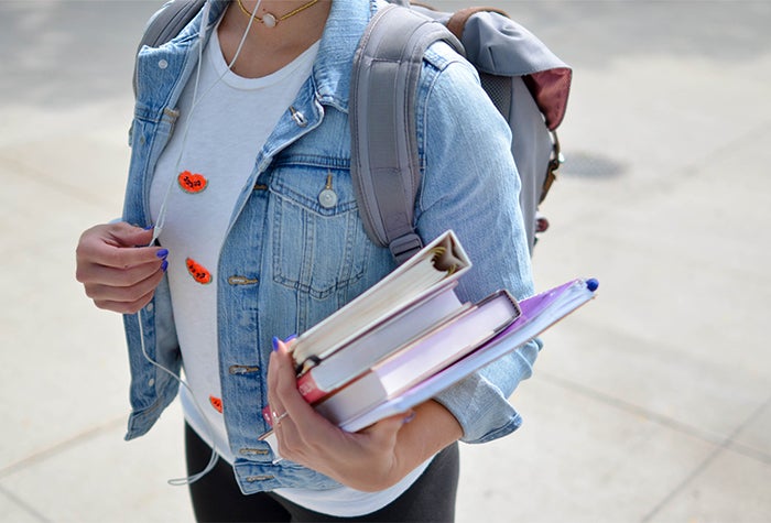 Student wearing jean jacket holding several textbooks in arm