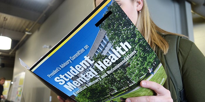 Student reading a brochure with the text "Student Mental Health" on it