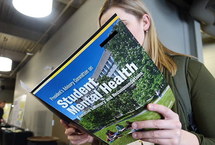 Student reading a textbook titled "Student Mental Health"