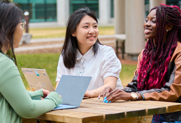 Students sitting at a table outsite on campus with their laptops open