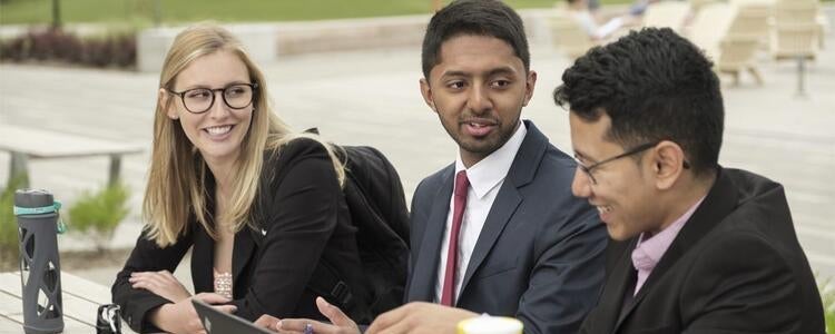 Three students sitting and smiling outside