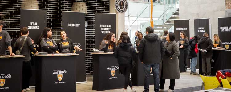 Group of people standing at a booth with a Faculty of Arts representative at it