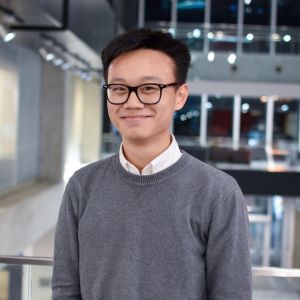 Jeffrey wears a collared sweater and glasses and smiles indoors