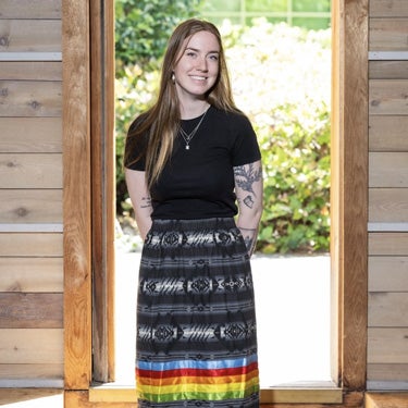Kylee smiles in front of a doorway wearing a ribbon skirt